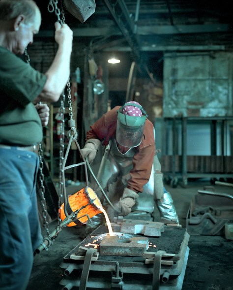 Pankratz pours molten metal into the form while Dave Olson watches.